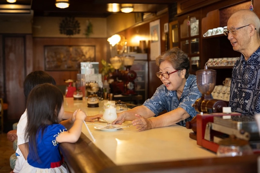 喫茶店のカウンター越しに飲み物を渡すかわいらしいおばあちゃん