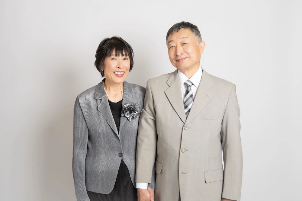 薄いグレーの壁の前で、笑顔で撮影されている老夫婦
