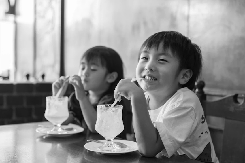 喫茶店で美味しそうにジュースを飲む二人の子供のモノクロ写真。カメラ目線