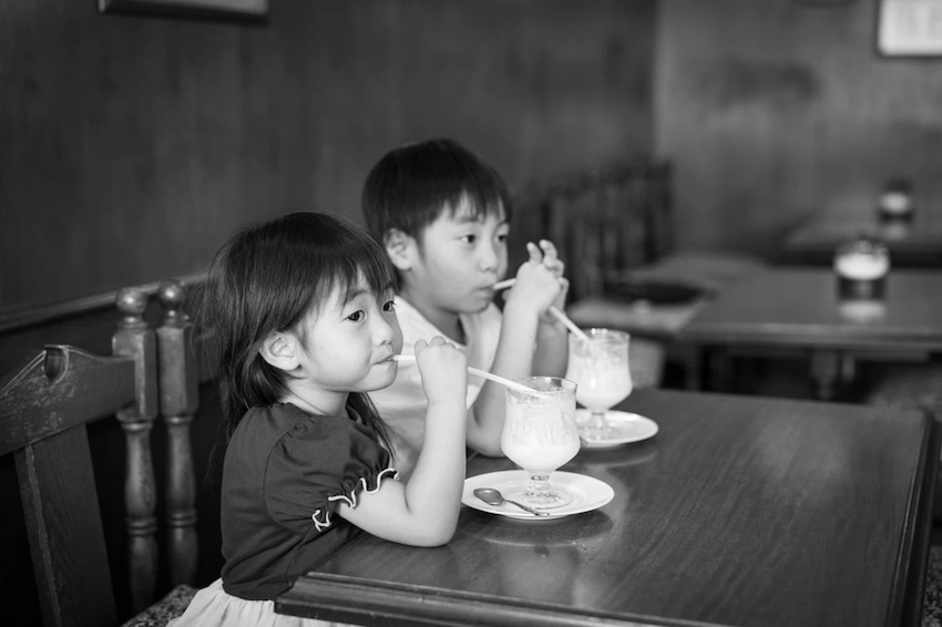 喫茶店で美味しそうにジュースを飲む二人の子供のモノクロ写真